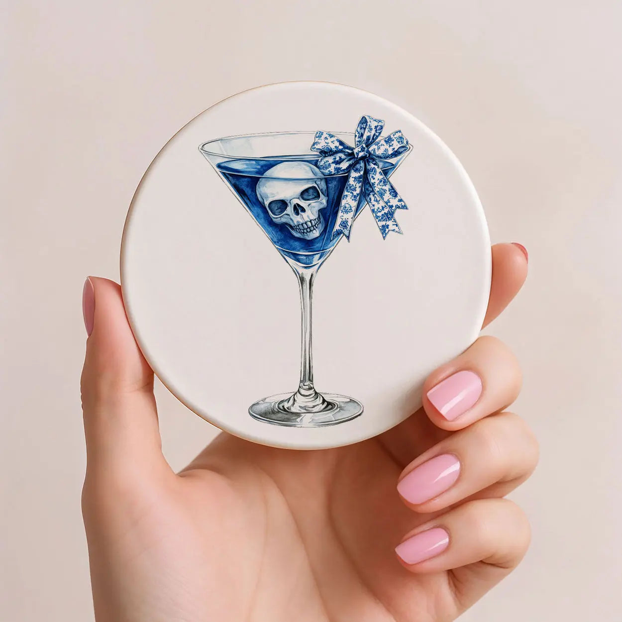 Round coaster with a skull in a blue martini glass design held by a hand.