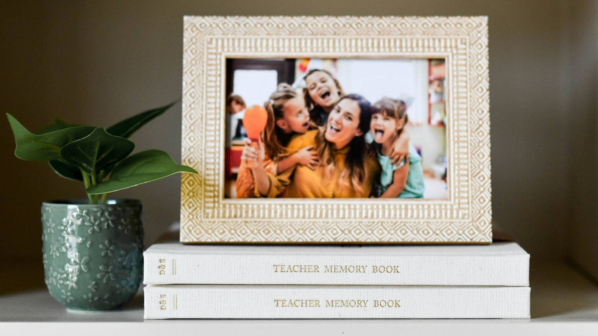 Decorative photo frame with a family photo on top of a 'Teacher Memory Book'.