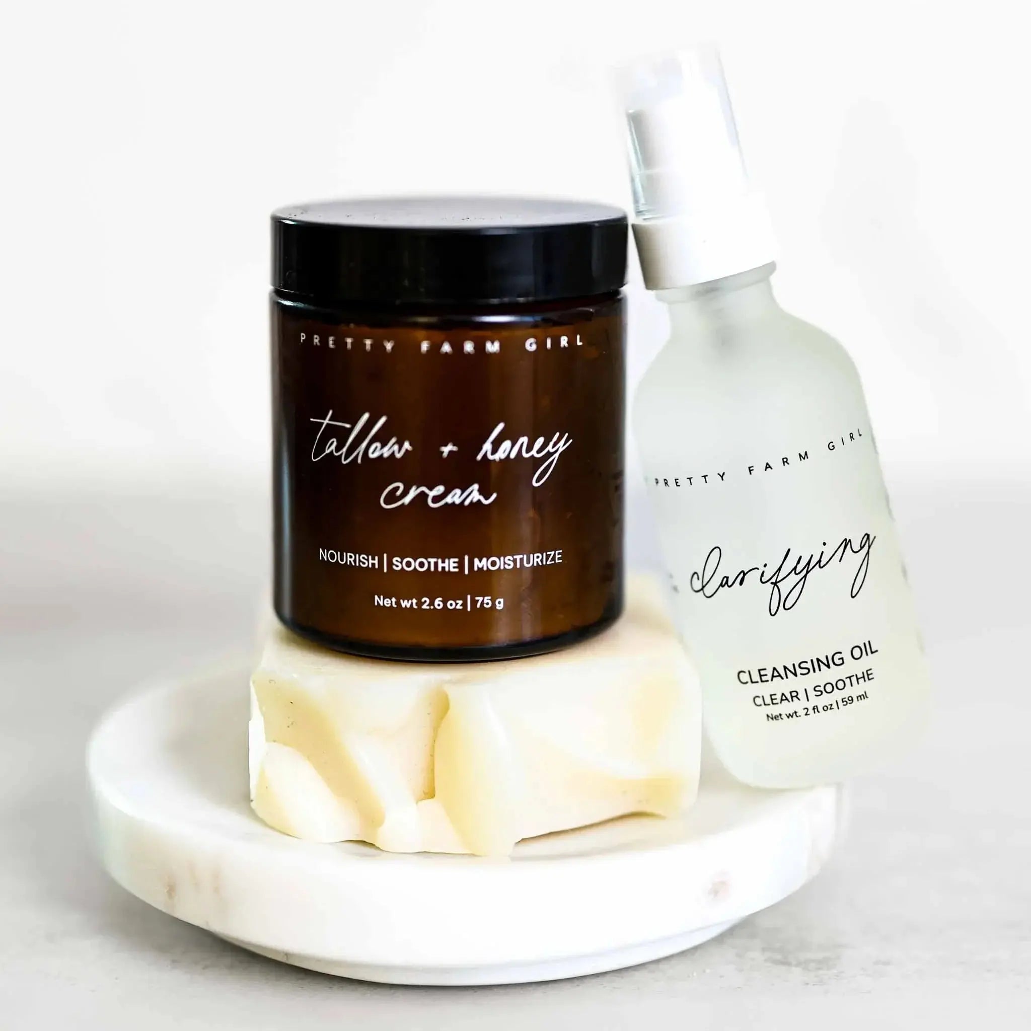 Tallow + honey cream and clarifying cleansing oil bath essentials on marble tray, cozy farmhouse skincare