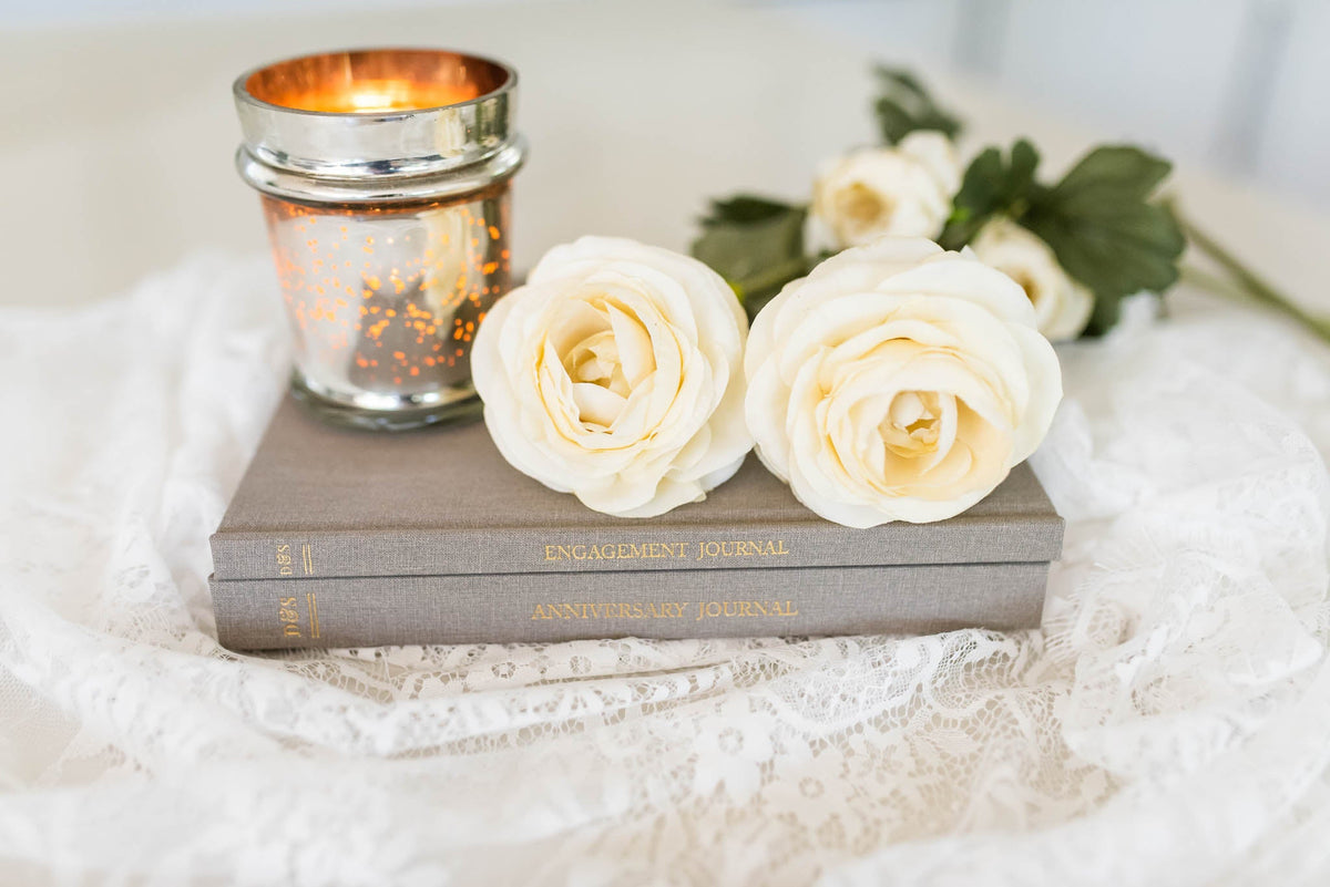 Engagement Journal and Anniversary Journal with a candle and roses. Sitting on top of a cream cloth