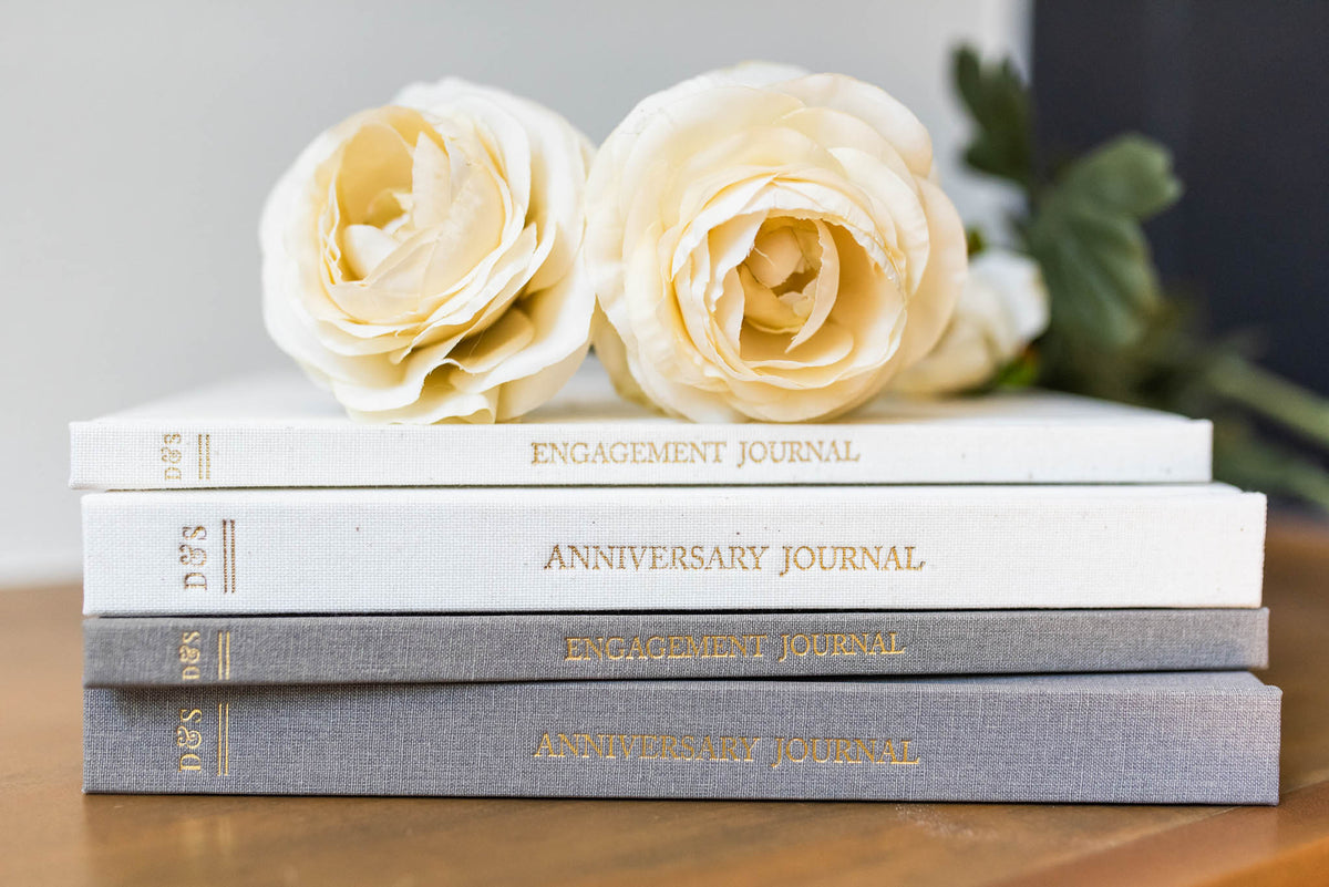 Anniversary and Engagement Journals in Ivory and Taupe with two Roses on top. Sitting on top of a table
