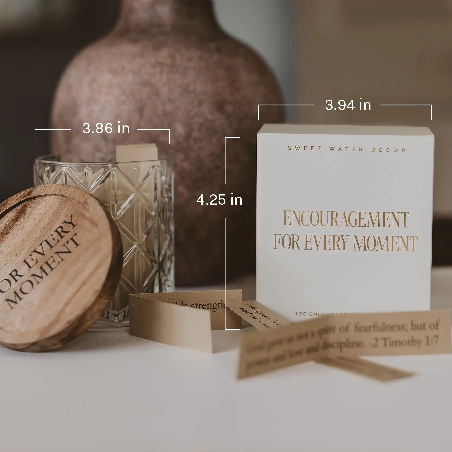 A boxed candle set labeled 'ENCOURAGEMENT FOR EVERY MOMENT' by Sweet Water Decor, shown with a white box, wooden lid, glass vessel, and small prayer cards on a tabletop. Measurement callouts indicate 3.