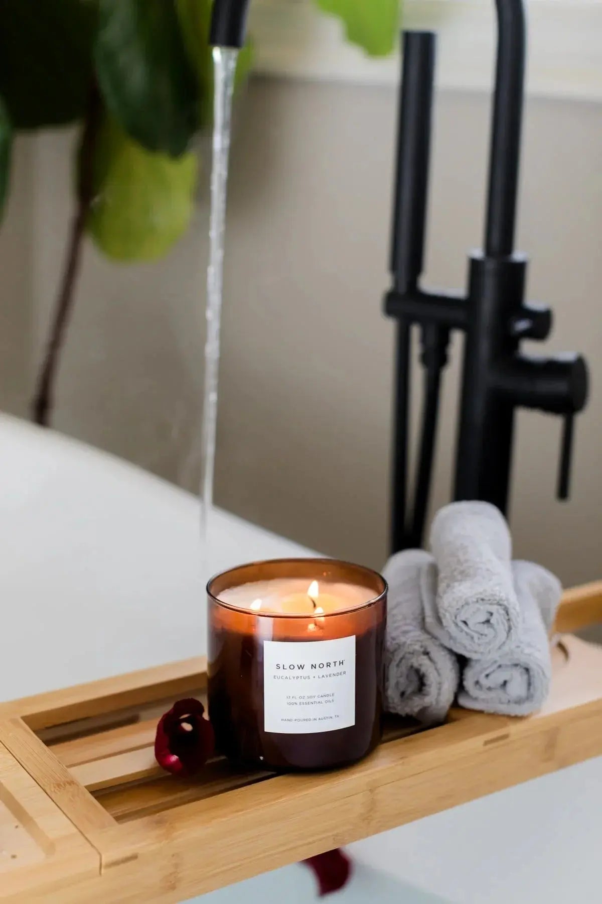 Lit eucalyptus lavender soy candle on bamboo bath tray with towels, perfect for cozy farmhouse bathroom decor