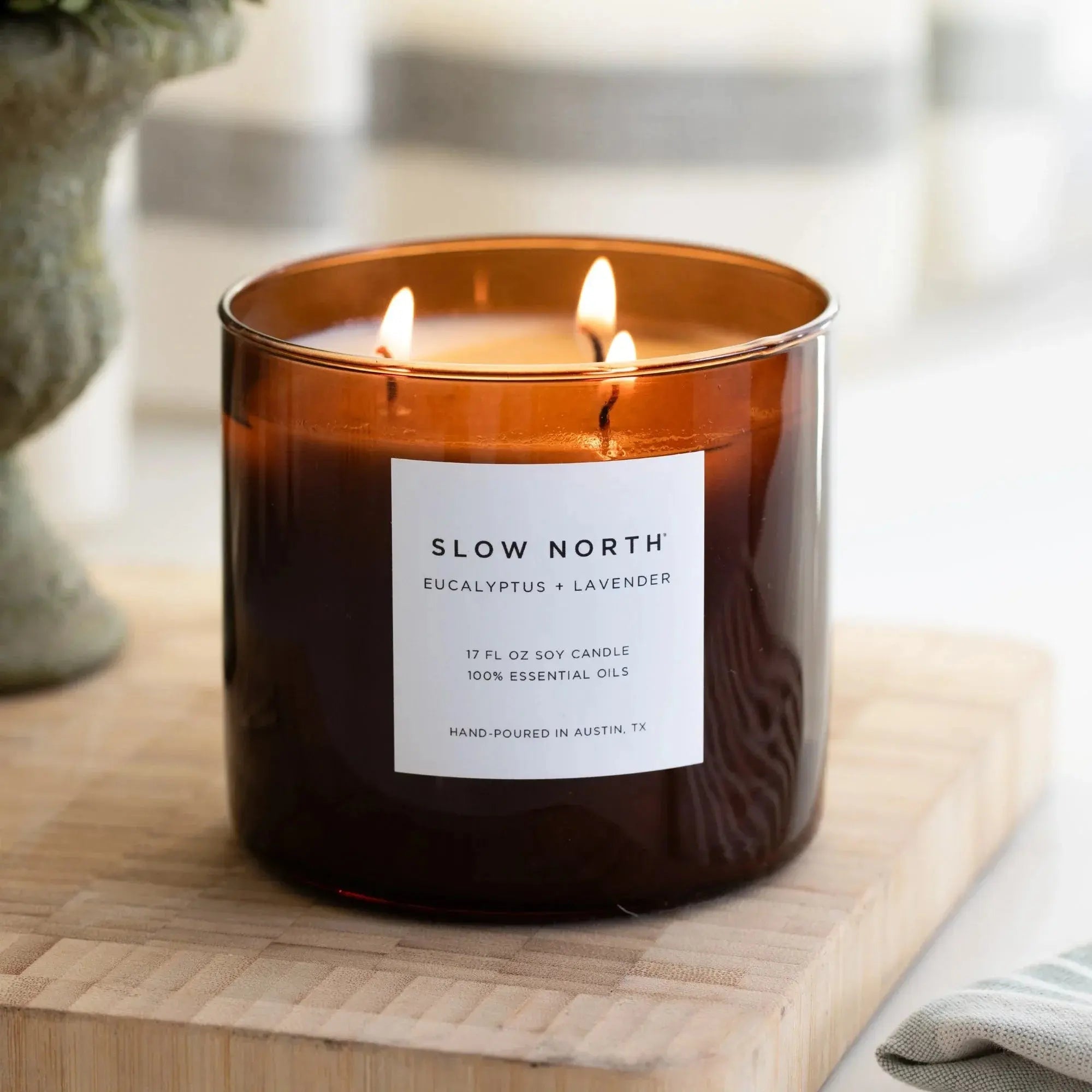 Slow North eucalyptus lavender soy candle in amber jar, lit with three wicks on wooden board