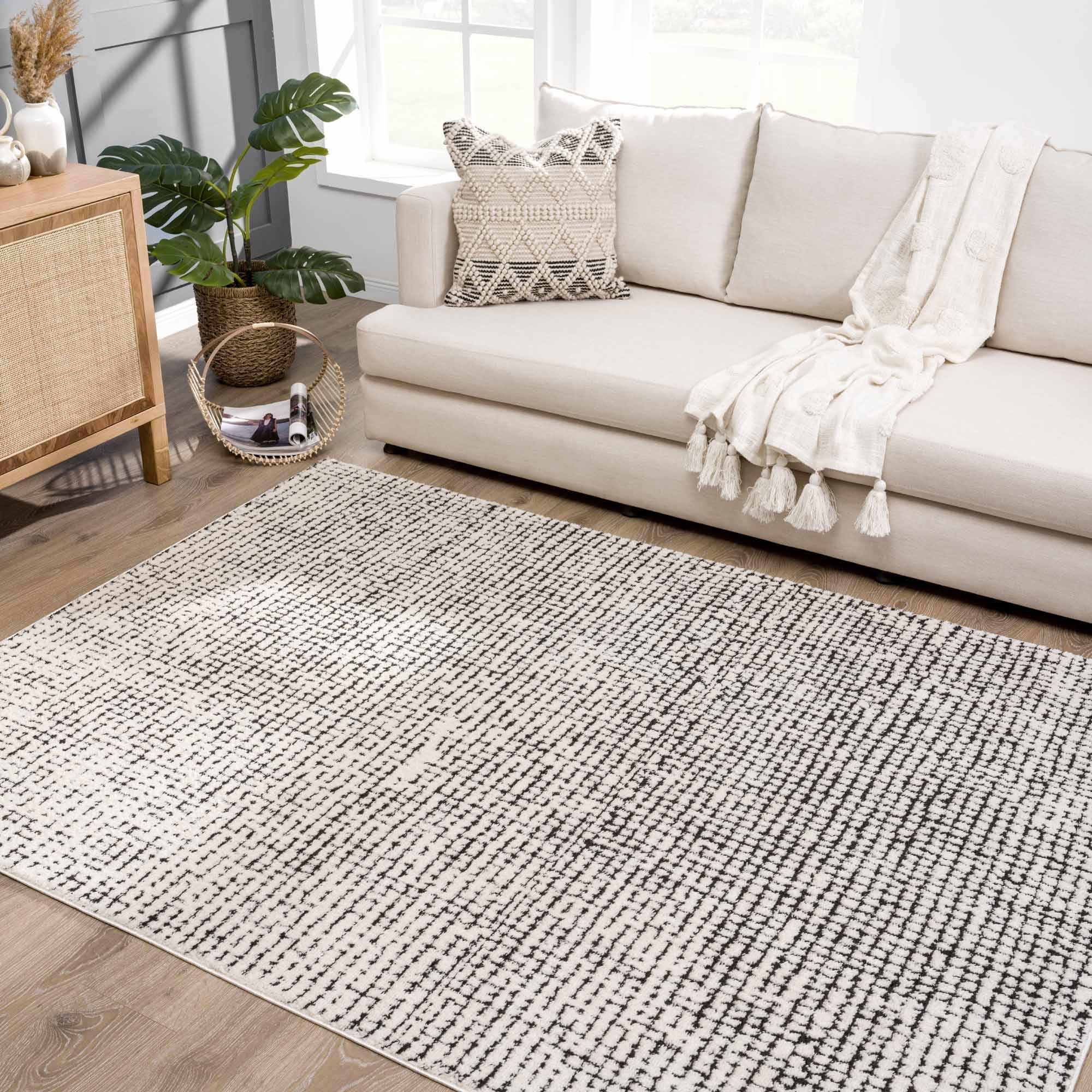 Cream and black geometric area rug in cozy farmhouse living room with sofa, tassel throw, and woven side table