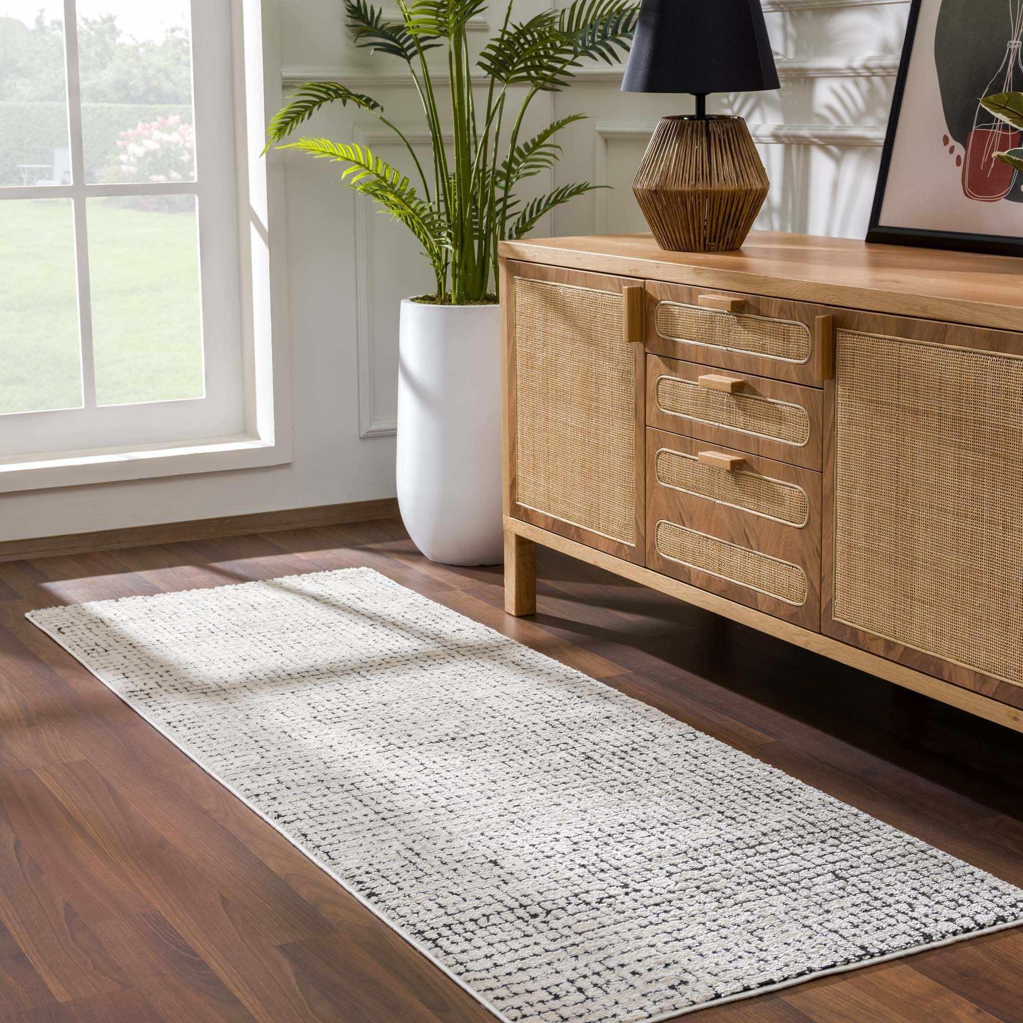 Cream textured area rug with black accents on hardwood floor, beside rattan cabinet and potted plant in cozy living room