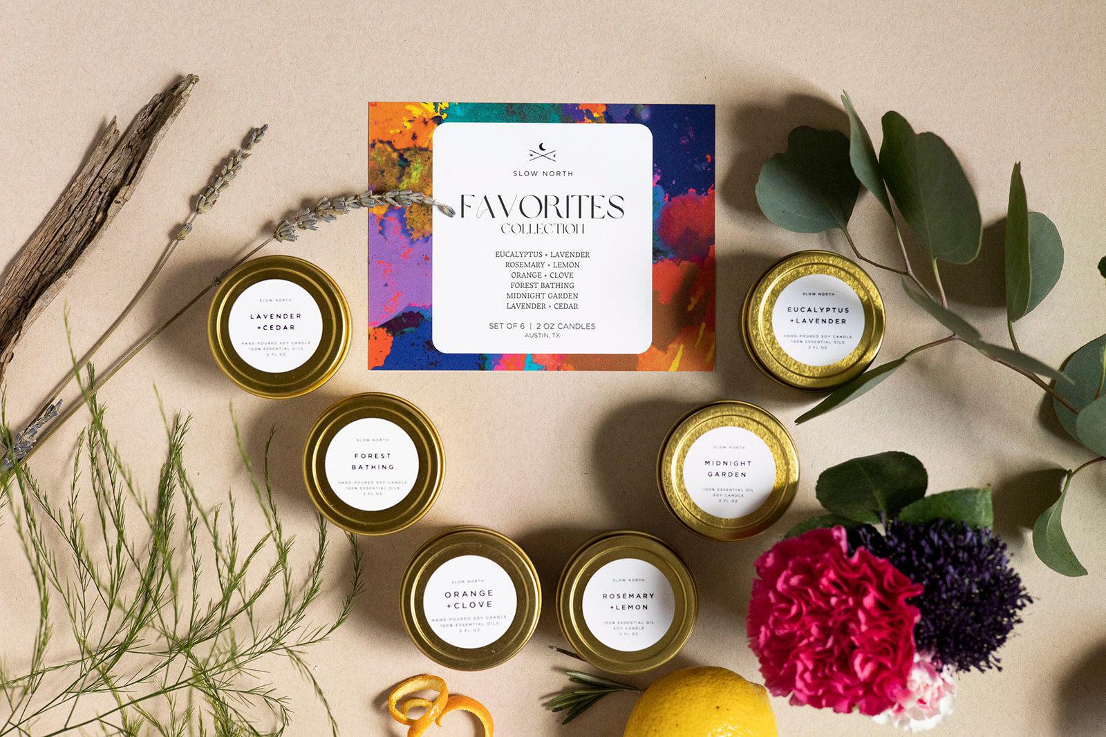 Collection of small candles with a colorful packaging label on a neutral background with plants and flowers.