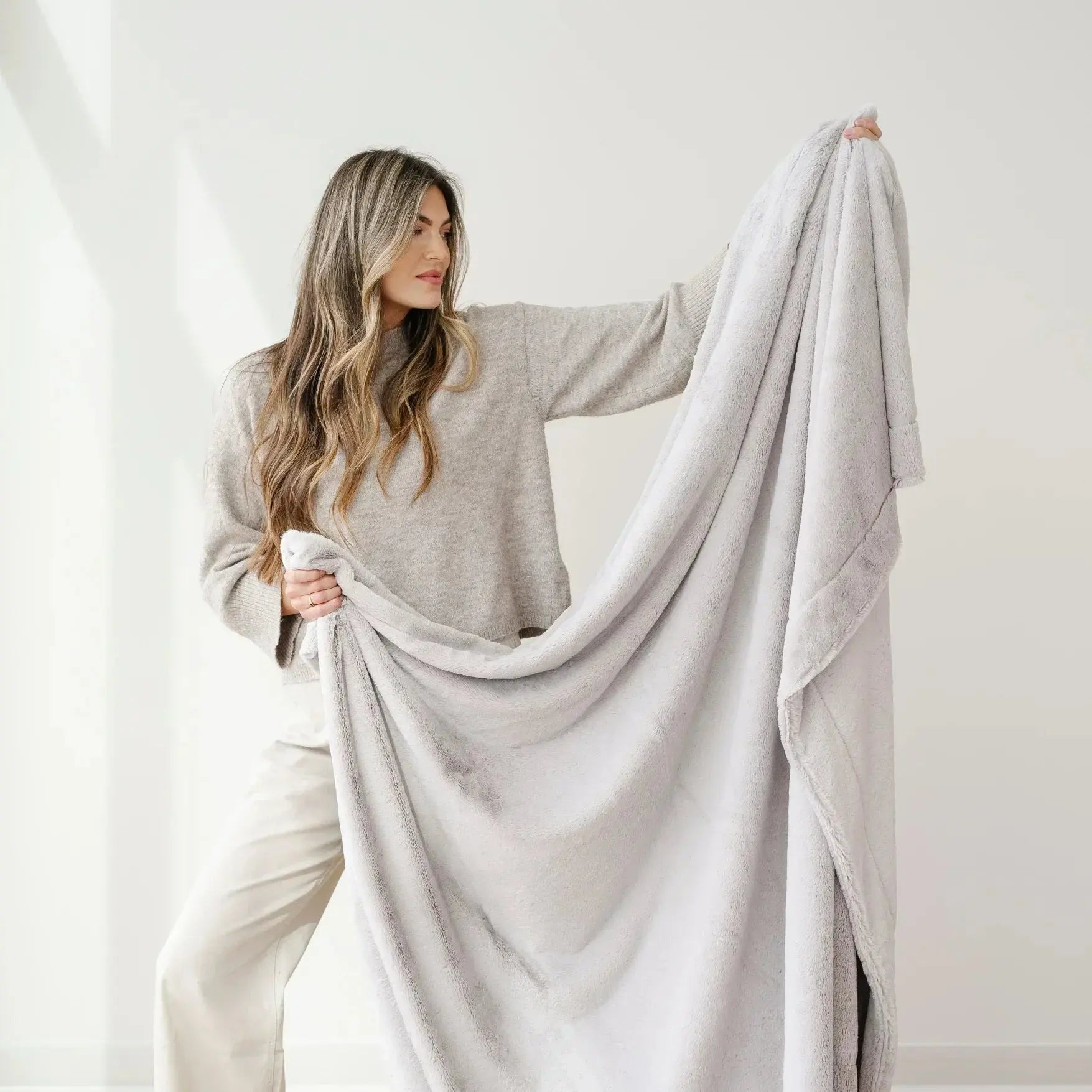 Woman holding a light gray blanket against a white background