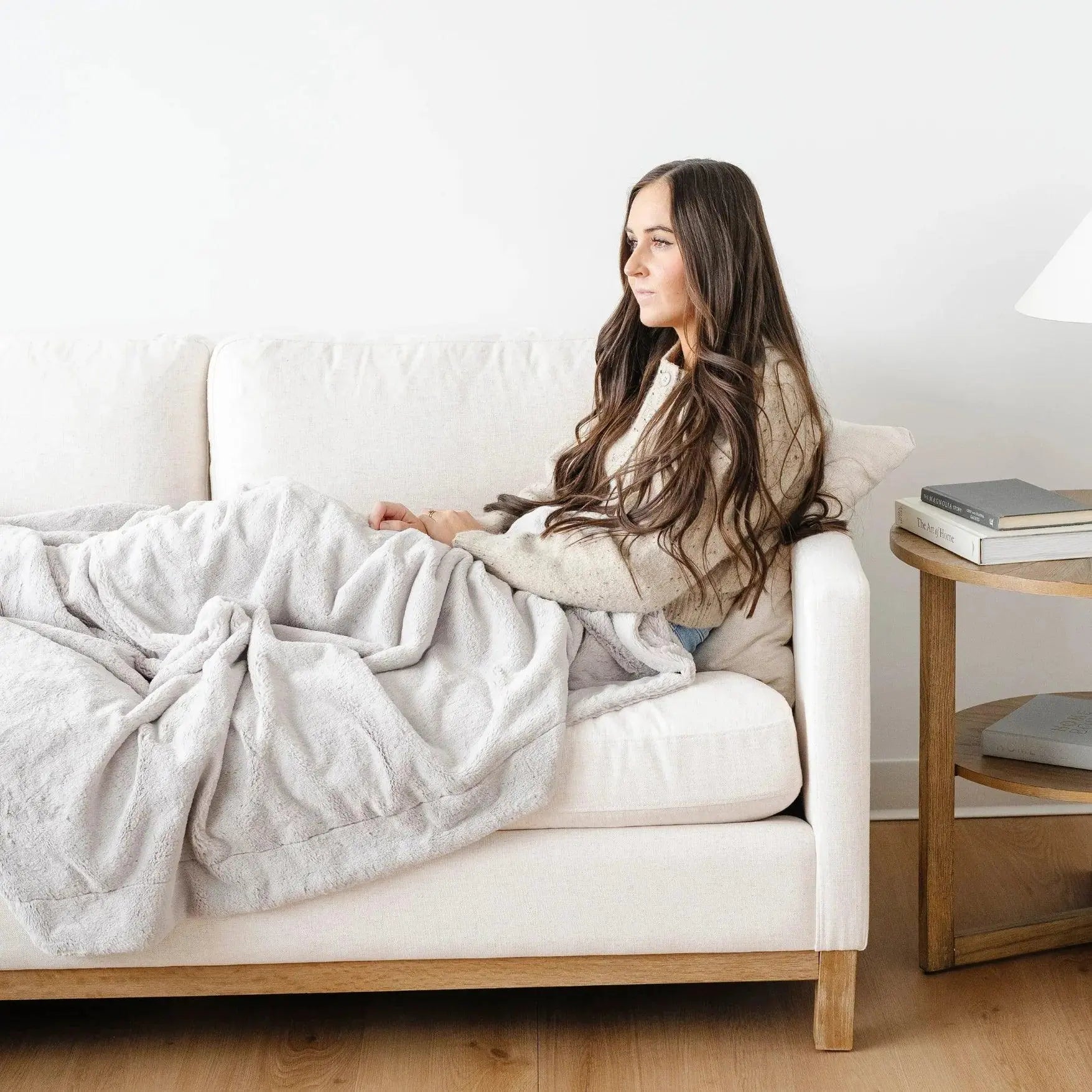 Woman sitting on a couch under a blanket in a cozy living room.