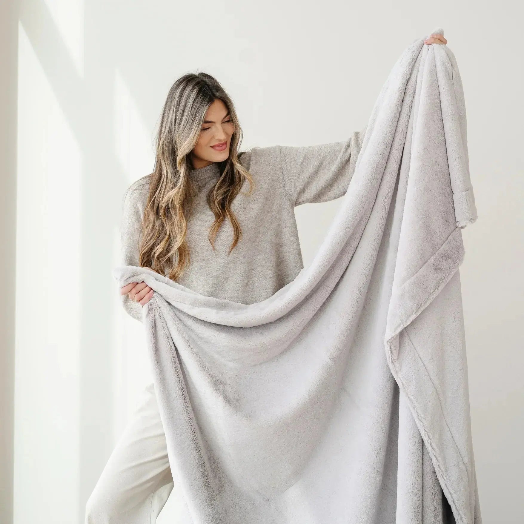 Woman holding a large light gray blanket against a white background