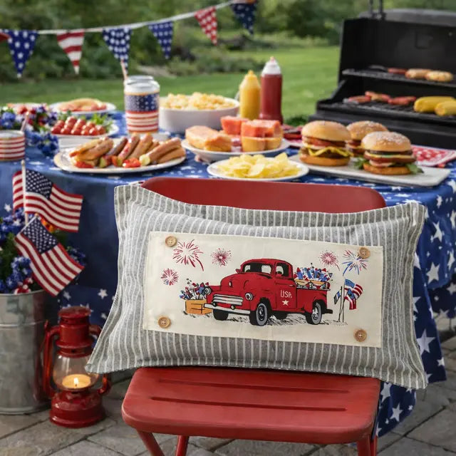Outdoor setting with a table of food, American flags, and a decorative pillow with a red truck design.