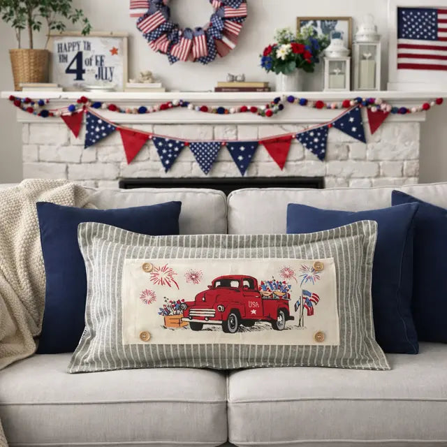 Decorative pillow with a red truck design on a couch, with a festive background featuring American flags and bunting.