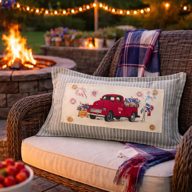 Decorative pillow with a red truck design on a wicker chair by a fire pit.
