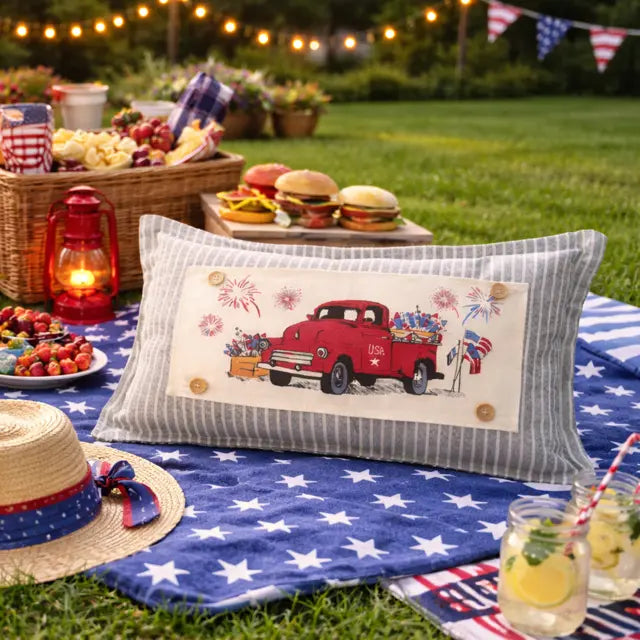 Picnic setup with a red truck pillow, food, and drinks on a grassy area.