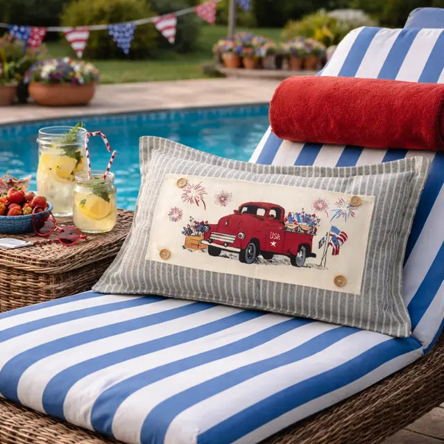 Chair with a decorative pillow featuring a red truck and American flags by a poolside.