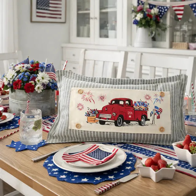 Dining table set for a patriotic celebration with a red truck pillow, American flags, and floral arrangements.