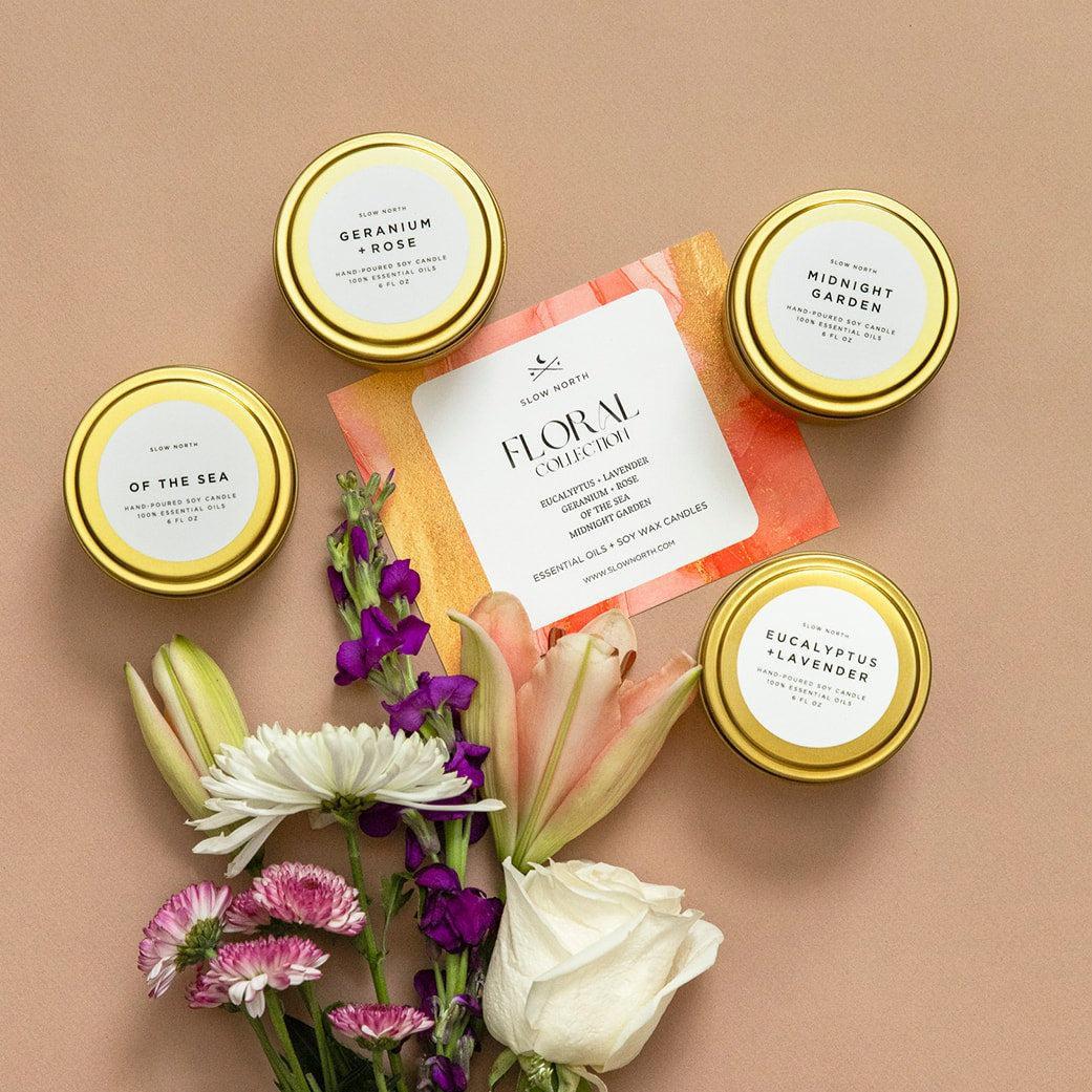 Four candles with gold lids and floral packaging on a beige background