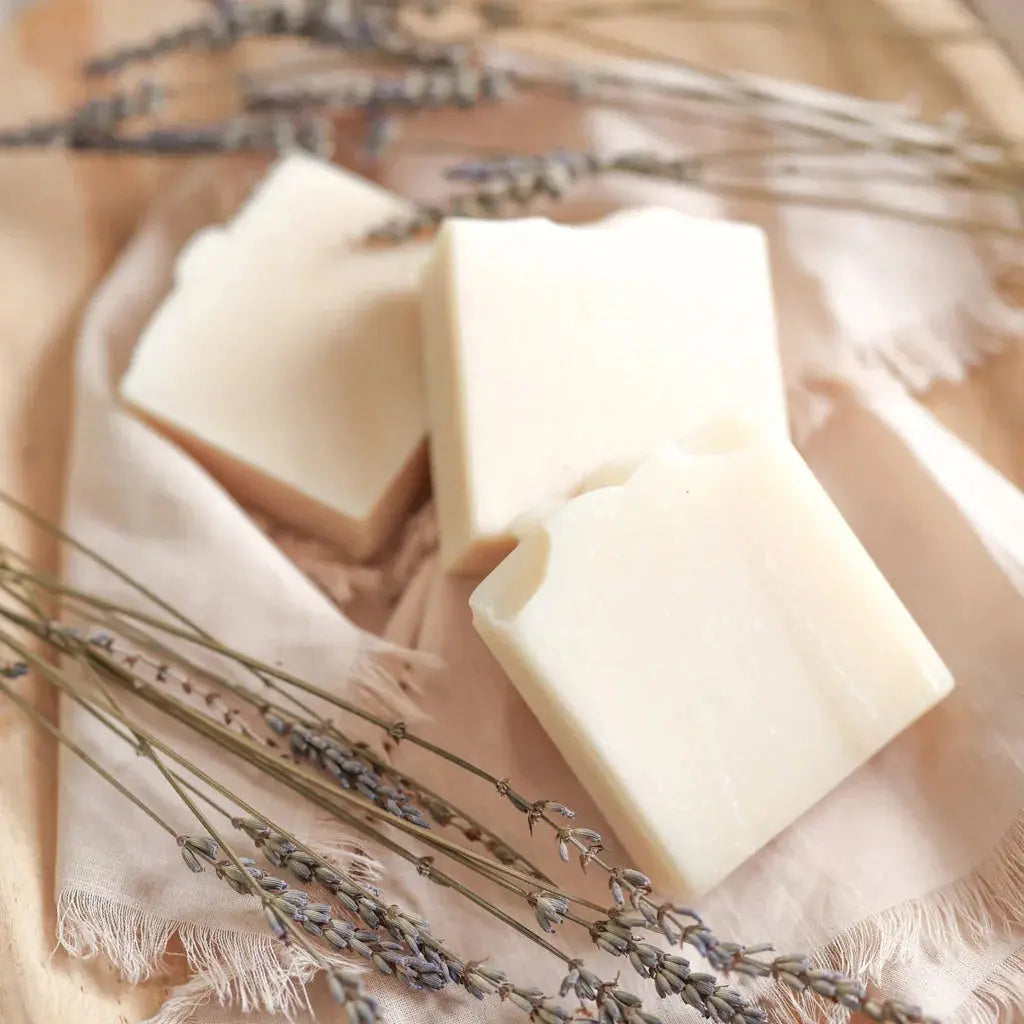 Creamy white farmhouse-style soap bars with dried lavender on soft linen, perfect for cozy bath essentials
