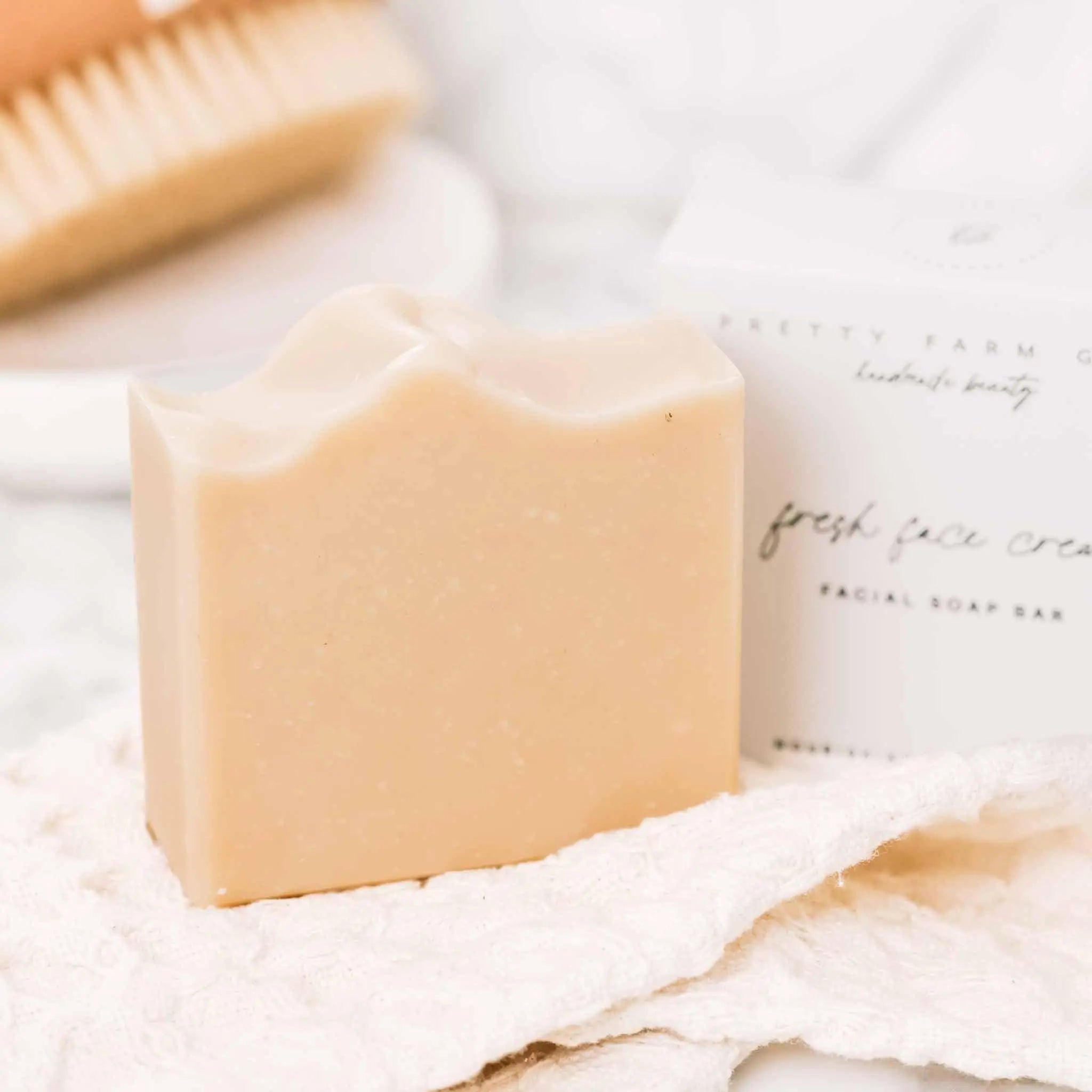 Creamy beige facial soap bar with wavy top, beside 'Fresh Face Cream' box, on white textured cloth