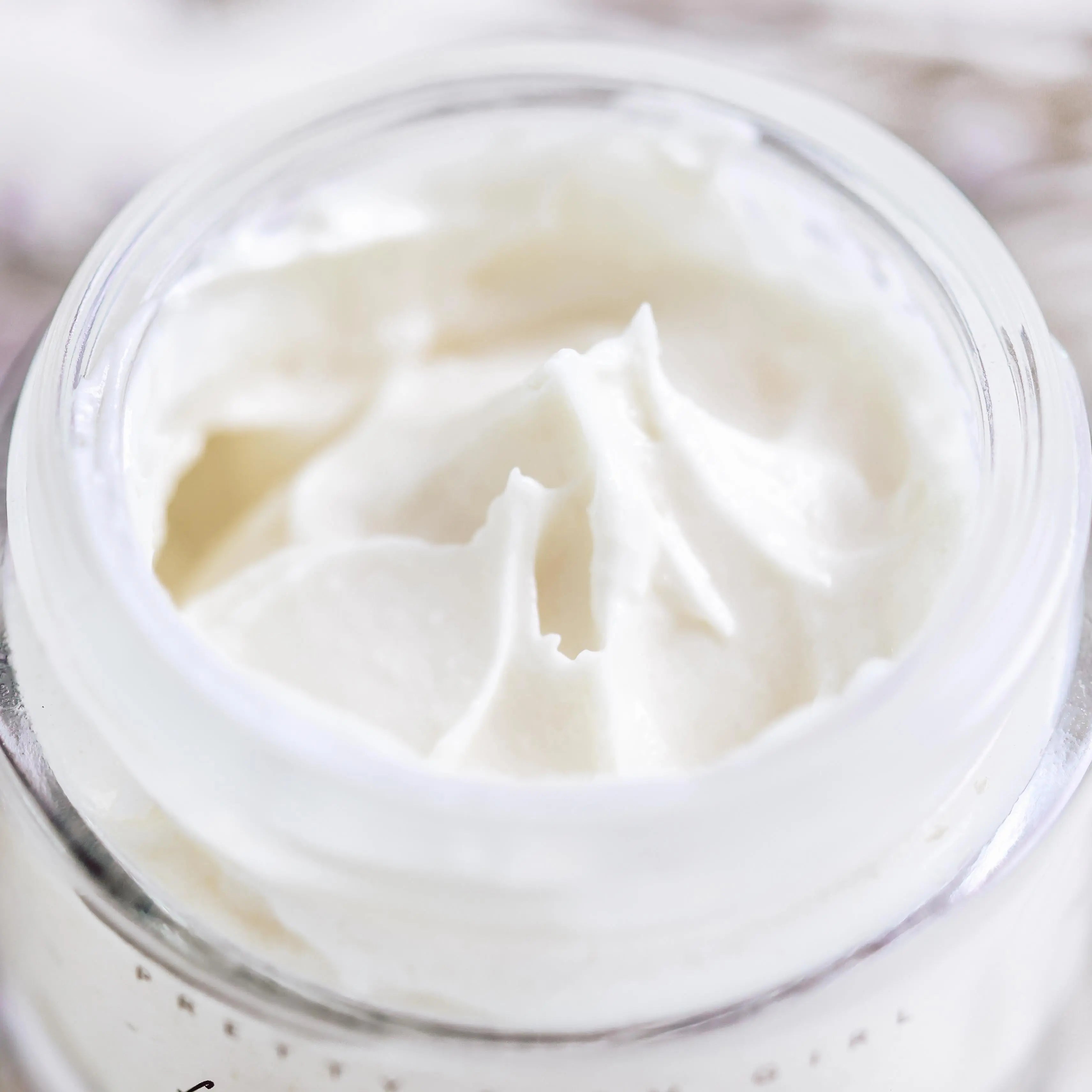 Creamy white body butter in a clear glass jar, perfect for cozy bath essentials and self-care routines.