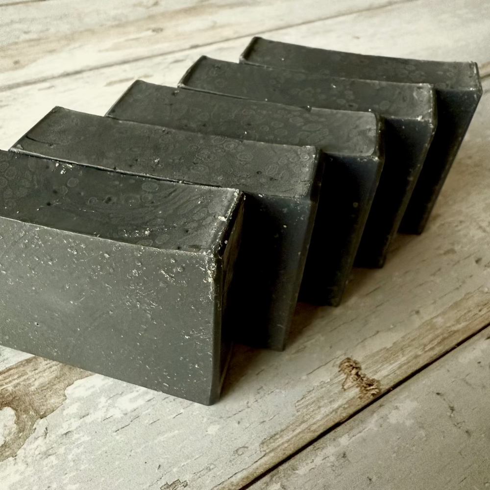 Five bars of black soap arranged on a wooden surface