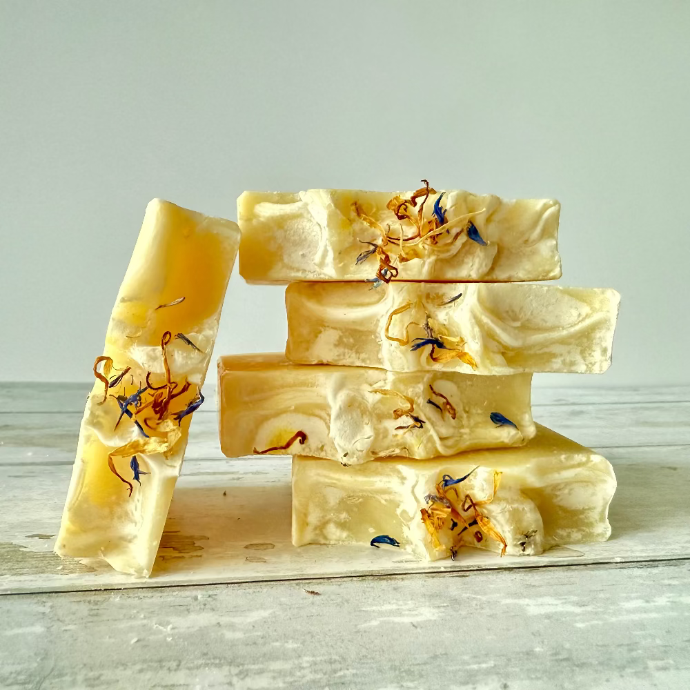 Stack of yellow soap bars with floral elements on a light wooden surface