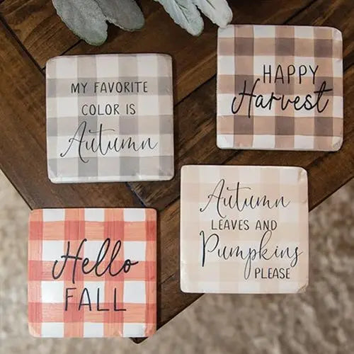 Set of four decorative coasters with autumn-themed text on a wooden surface.