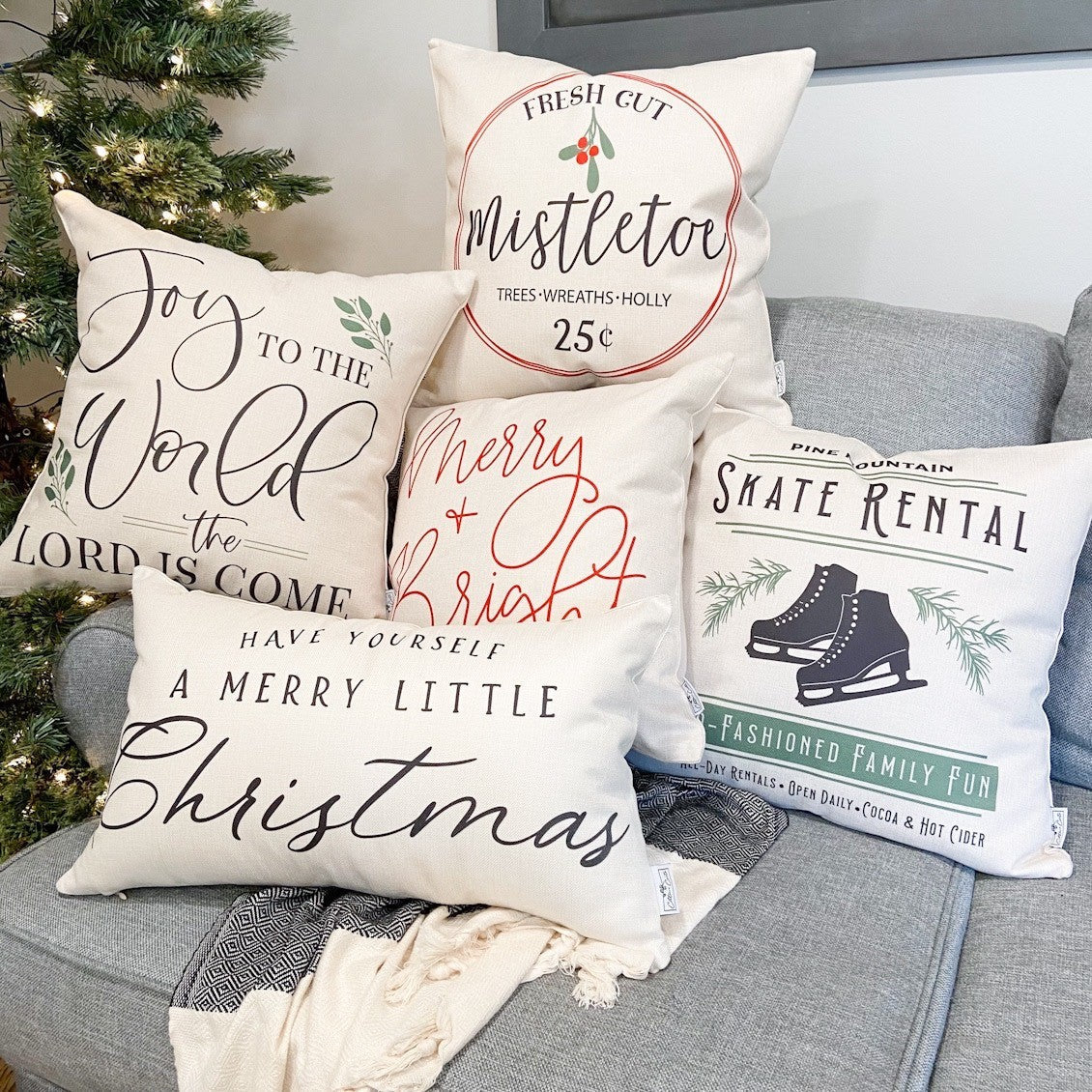 Decorative Christmas pillows on a gray couch with a Christmas tree in the background.
