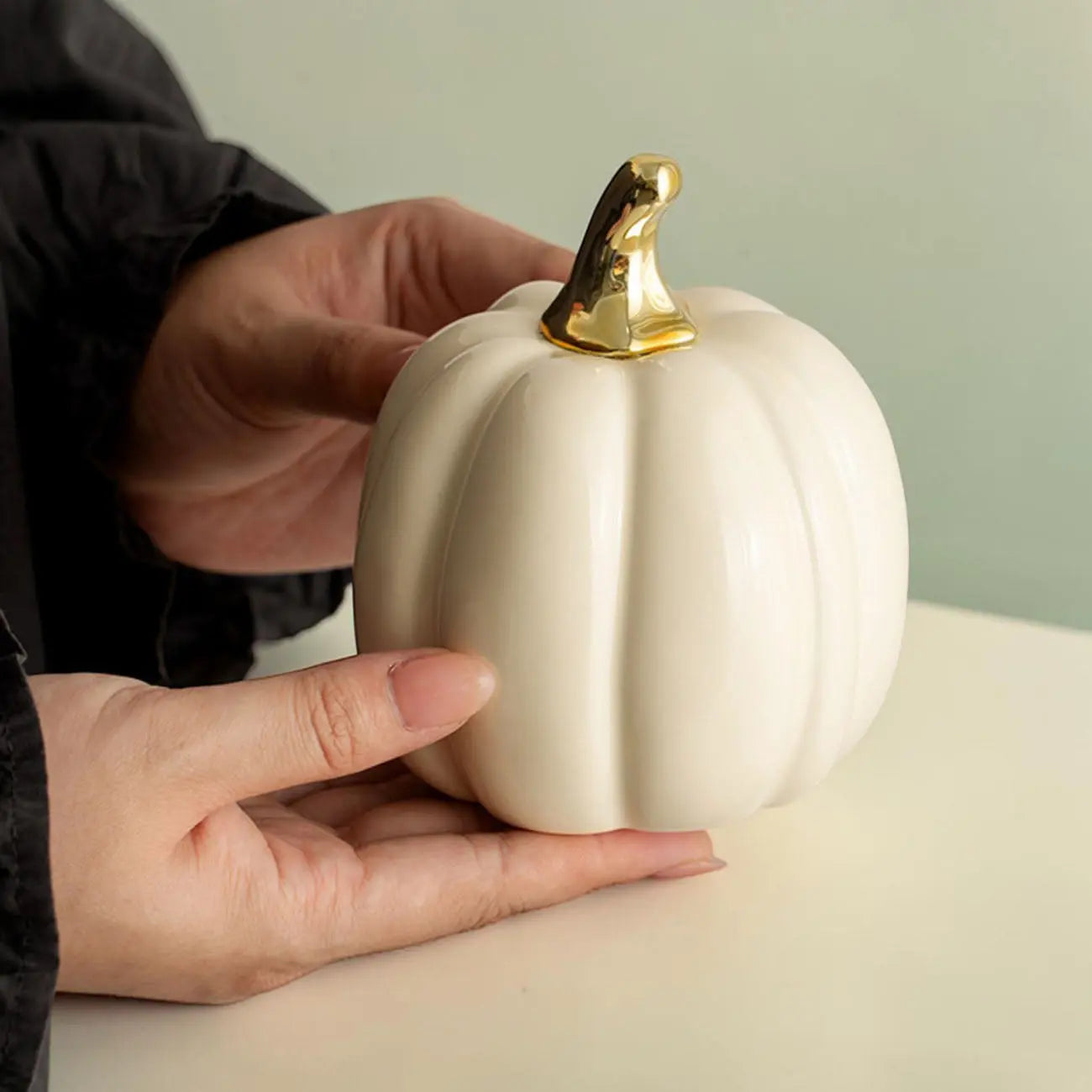 White pumpkin with a gold stem held by a person against a light green background