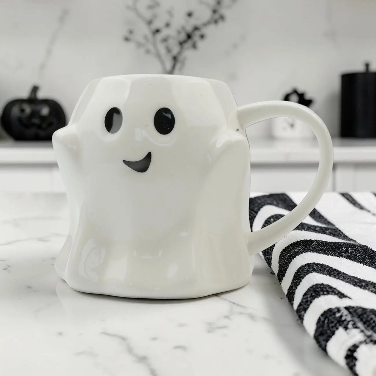 Ghost-shaped mug on a marble surface with Halloween decorations in the background
