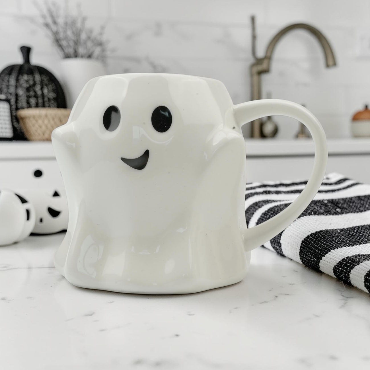 White ghost-shaped mug with black eyes and mouth on a marble countertop.