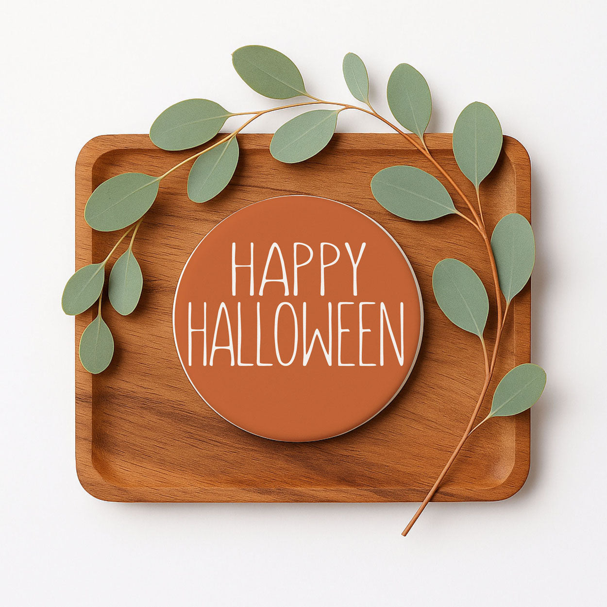 Wooden tray with a 'Happy Halloween' sign and green leaves on a white background