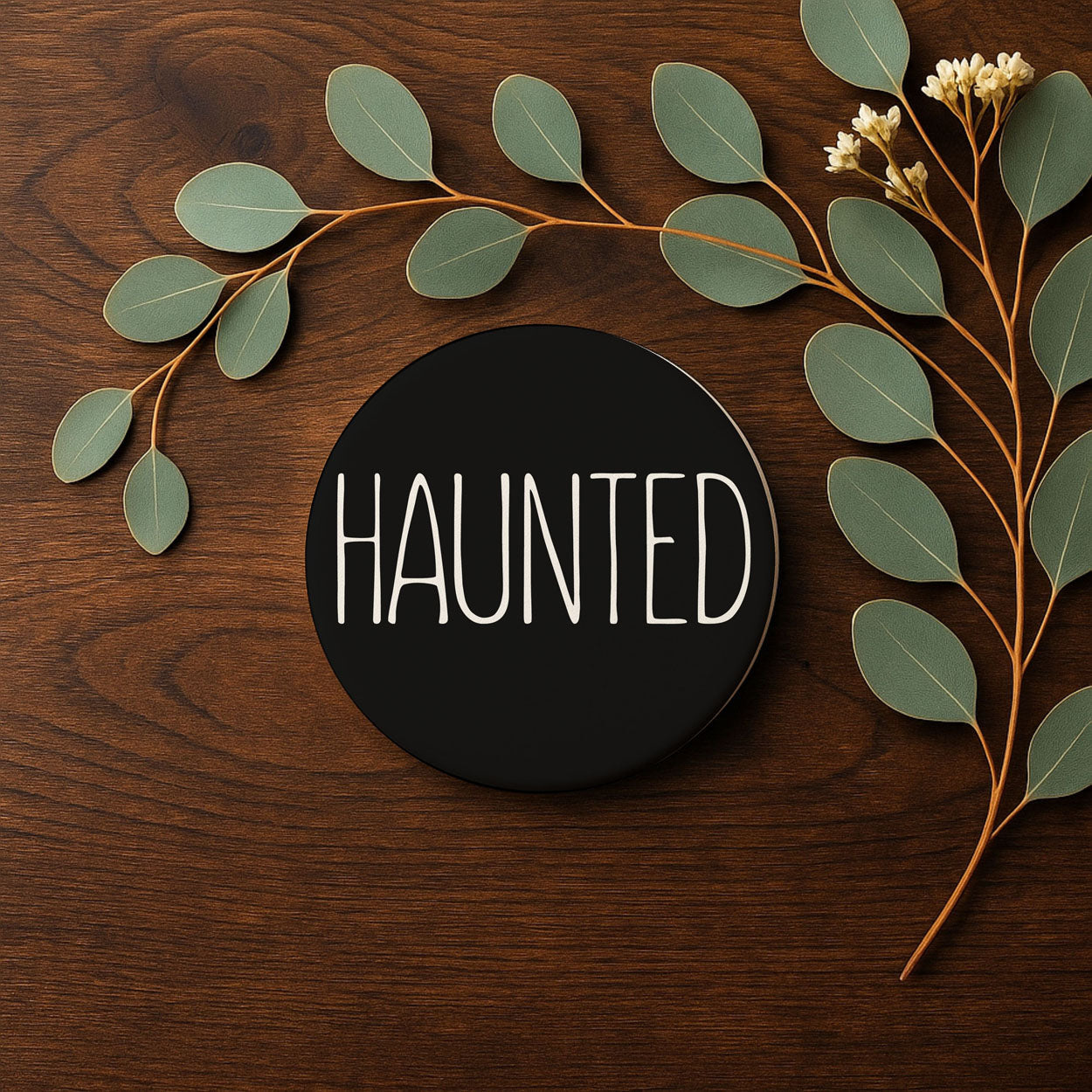 Decorative arrangement with leaves and a black circle displaying the word 'HAUNTED' on a wooden background.