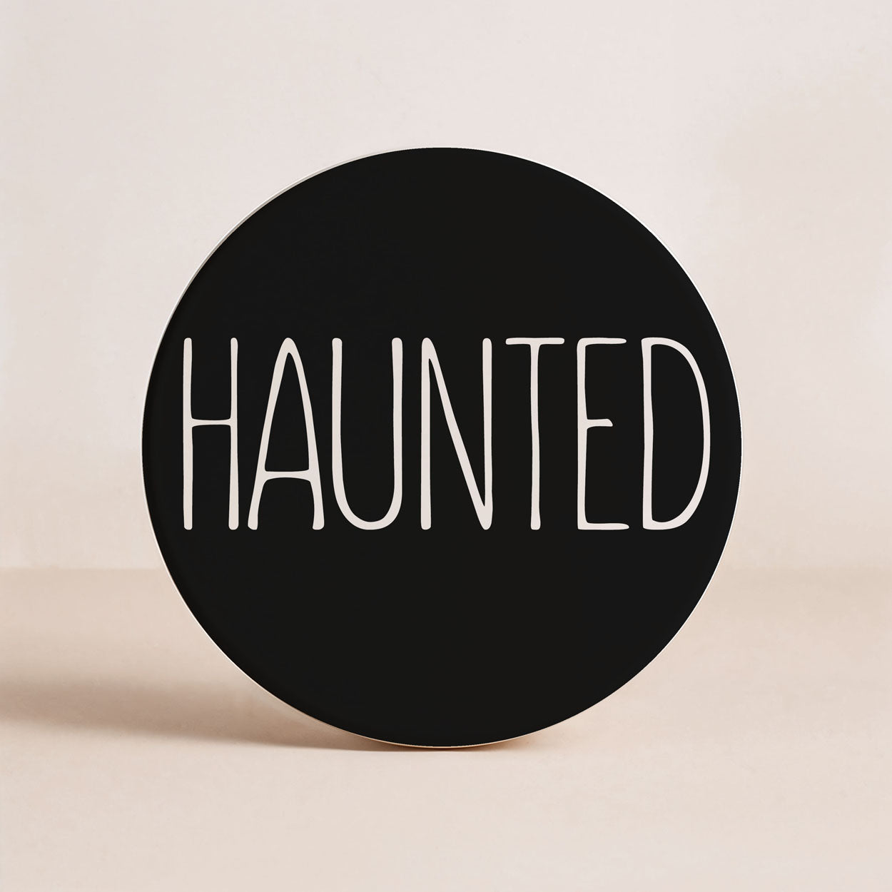 Round black sign with 'HAUNTED' text on a beige background