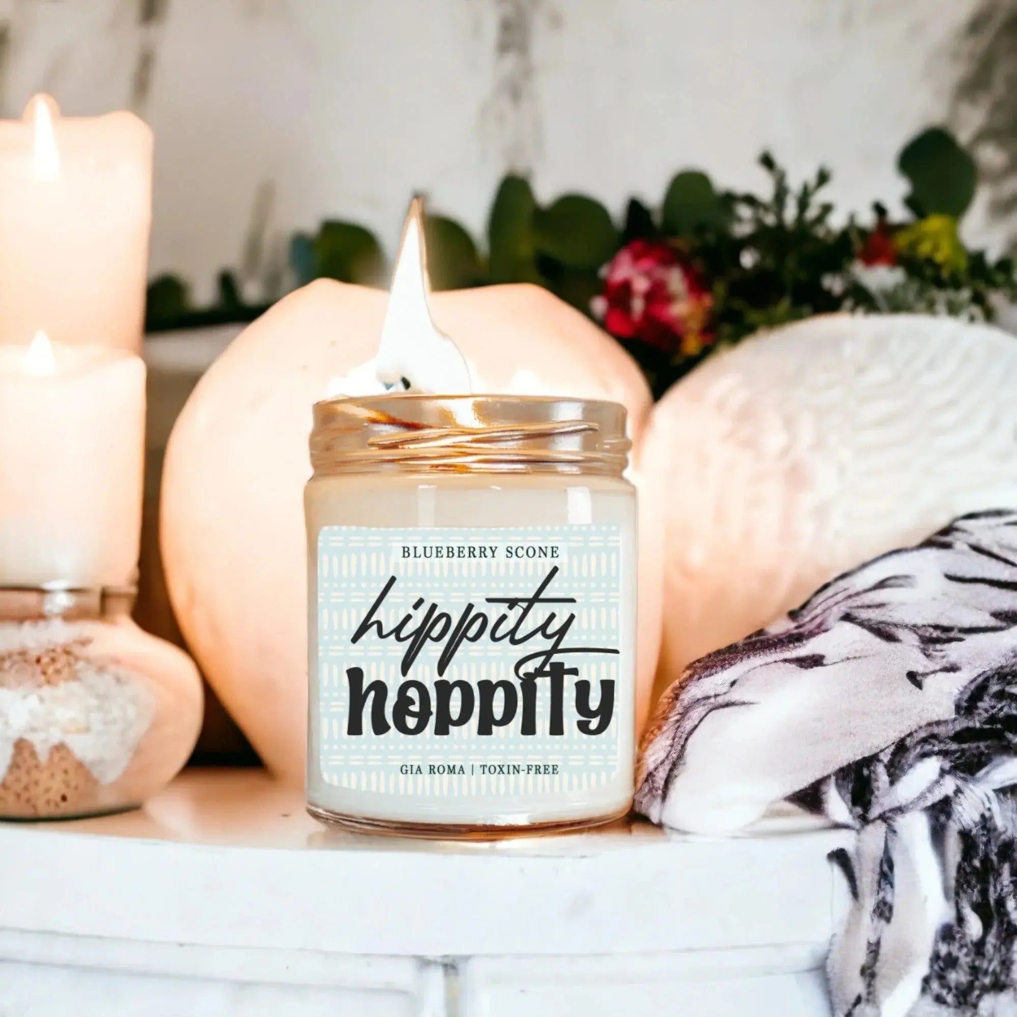Candle with 'hippity hippity' label on a decorative surface with pumpkins and greenery.