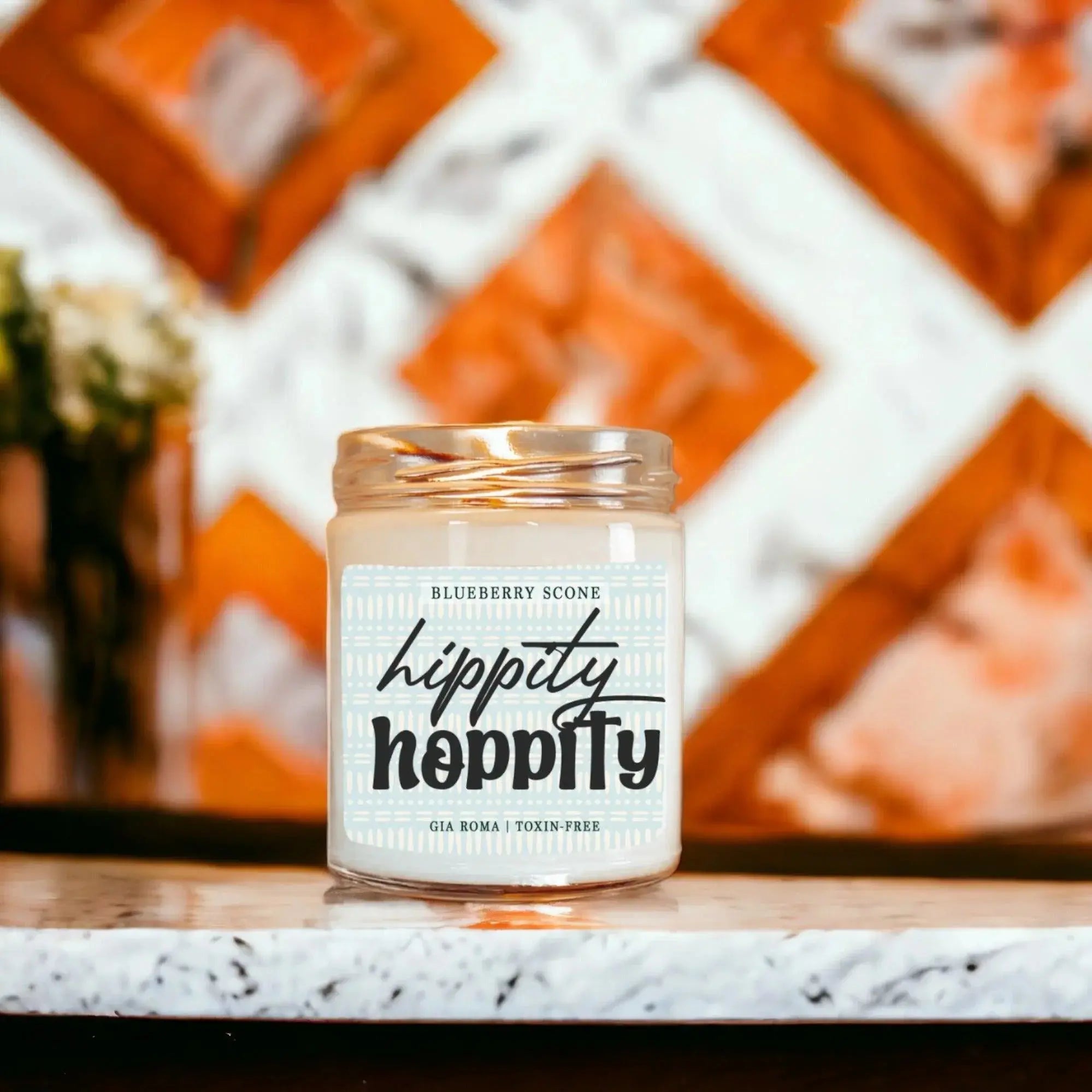 Candle jar labeled 'hippity hippity' on a marble surface with a decorative background