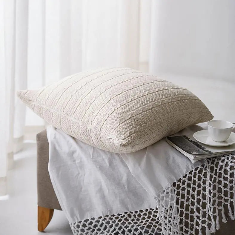 Cozy cream cable knit pillow on farmhouse-style bench with lace throw and teacup