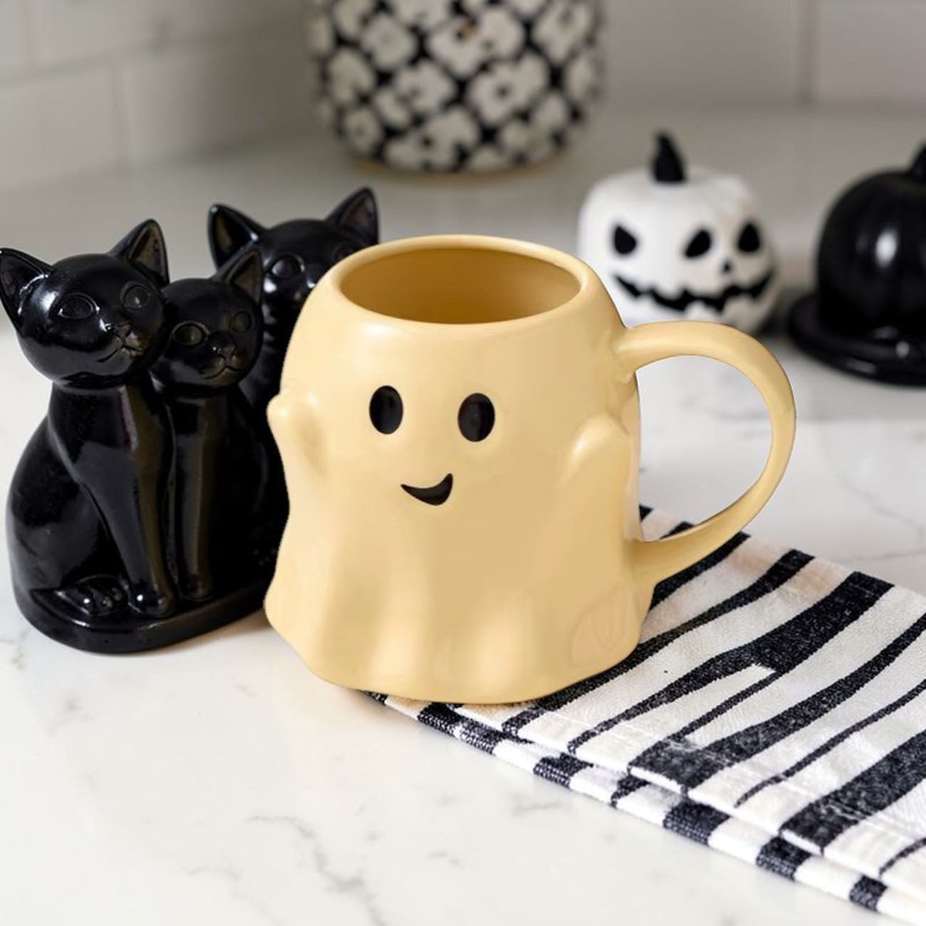 Ghost-shaped mug on a marble surface with Halloween decor in the background