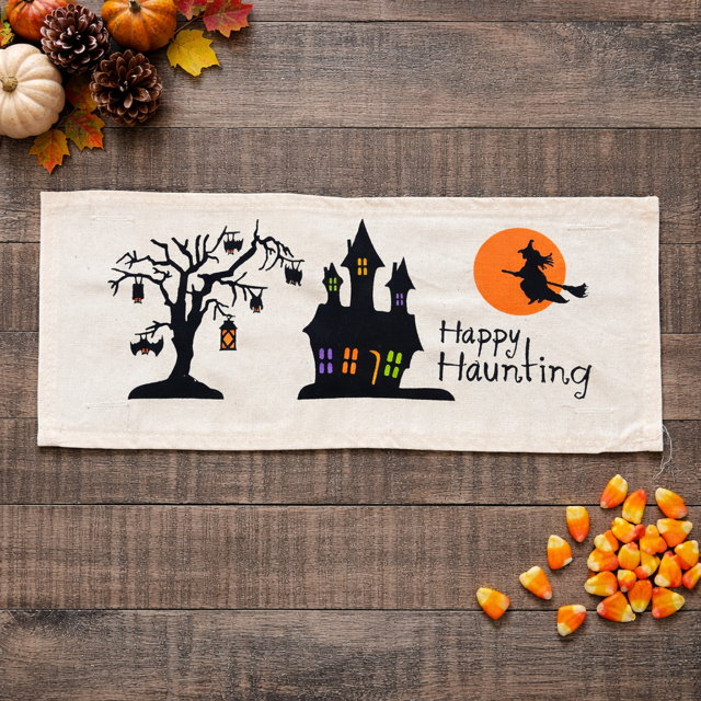 Halloween-themed decorative banner with a haunted house, tree, and witch on a wooden surface with pumpkins and cornucopia.