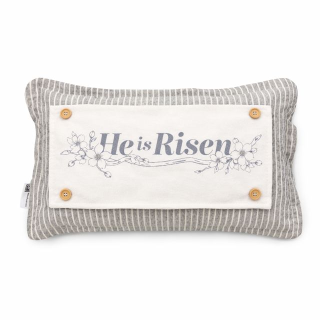 A rectangular decorative pillow with a gray and white striped fabric body, featuring a central cream fabric panel with the words 'He is Risen' in gray script, delicate floral line art, and four wooden buttons in the corners.