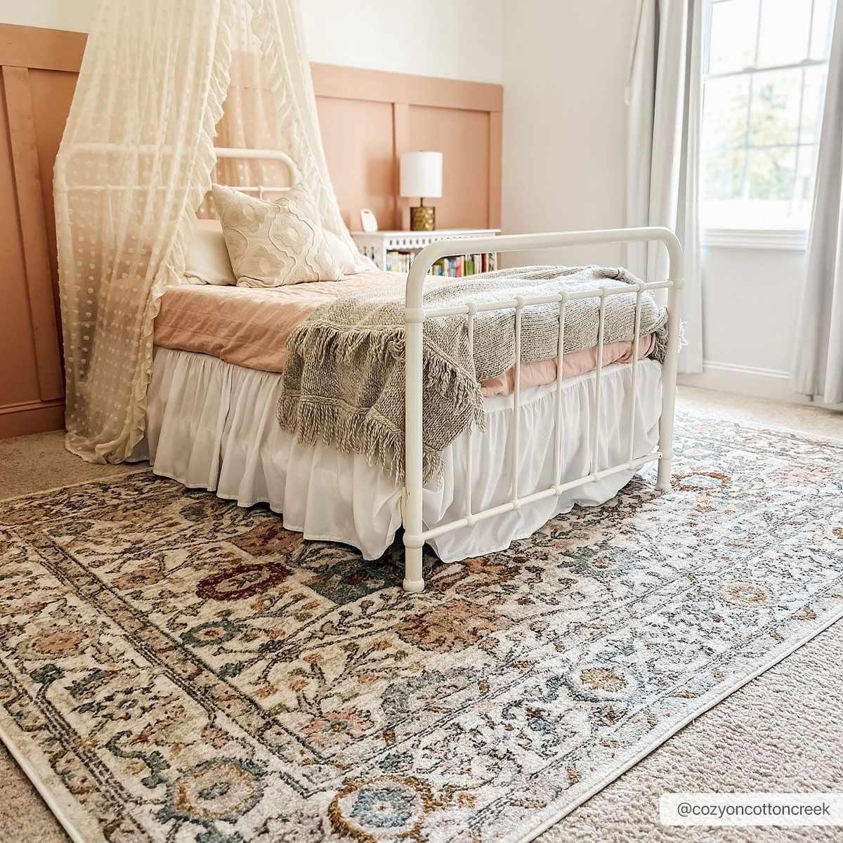 Cozy farmhouse bedroom with white iron bed, lace canopy, and vintage rug for warm cottage decor