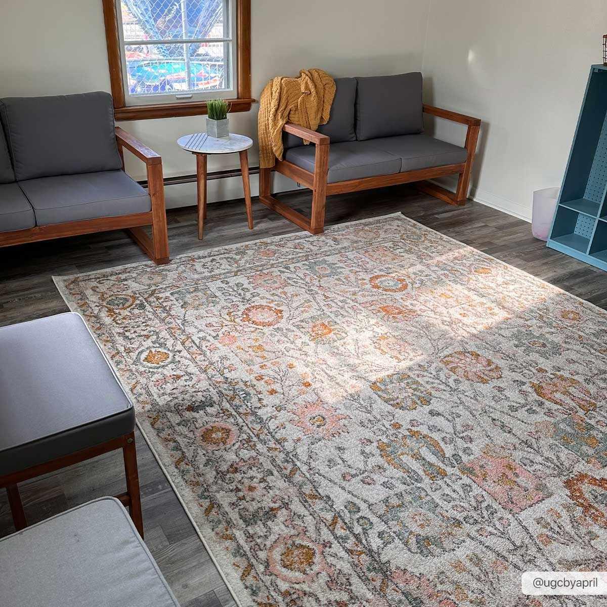 Cozy farmhouse living room with gray sofas, wooden furniture, and a vintage floral area rug for warm, peaceful home decor.