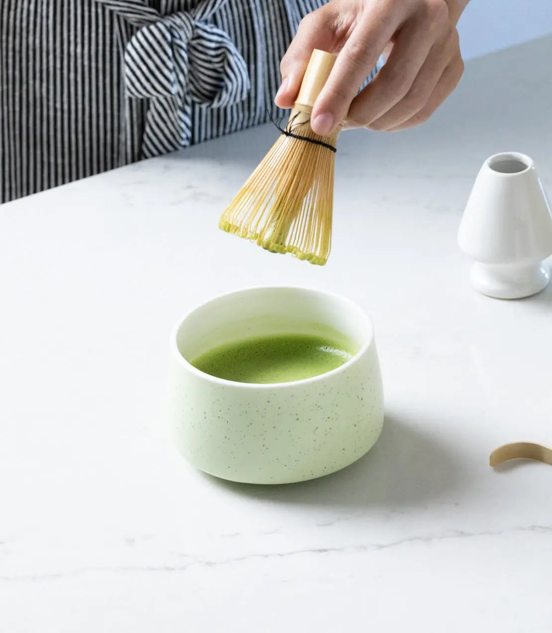 Hand whisking matcha in speckled ceramic bowl with bamboo whisk, cozy farmhouse kitchen decor