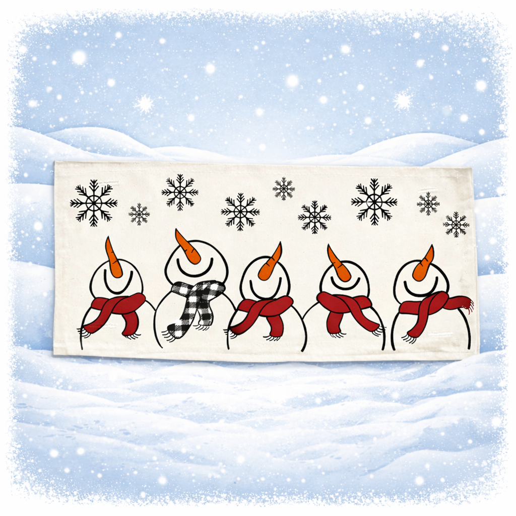 A rectangular cream-colored fabric napkin or tea towel featuring a winter illustration of five snowmen holding red scarves under black snowflakes, set against a snowy blue background with a white border.