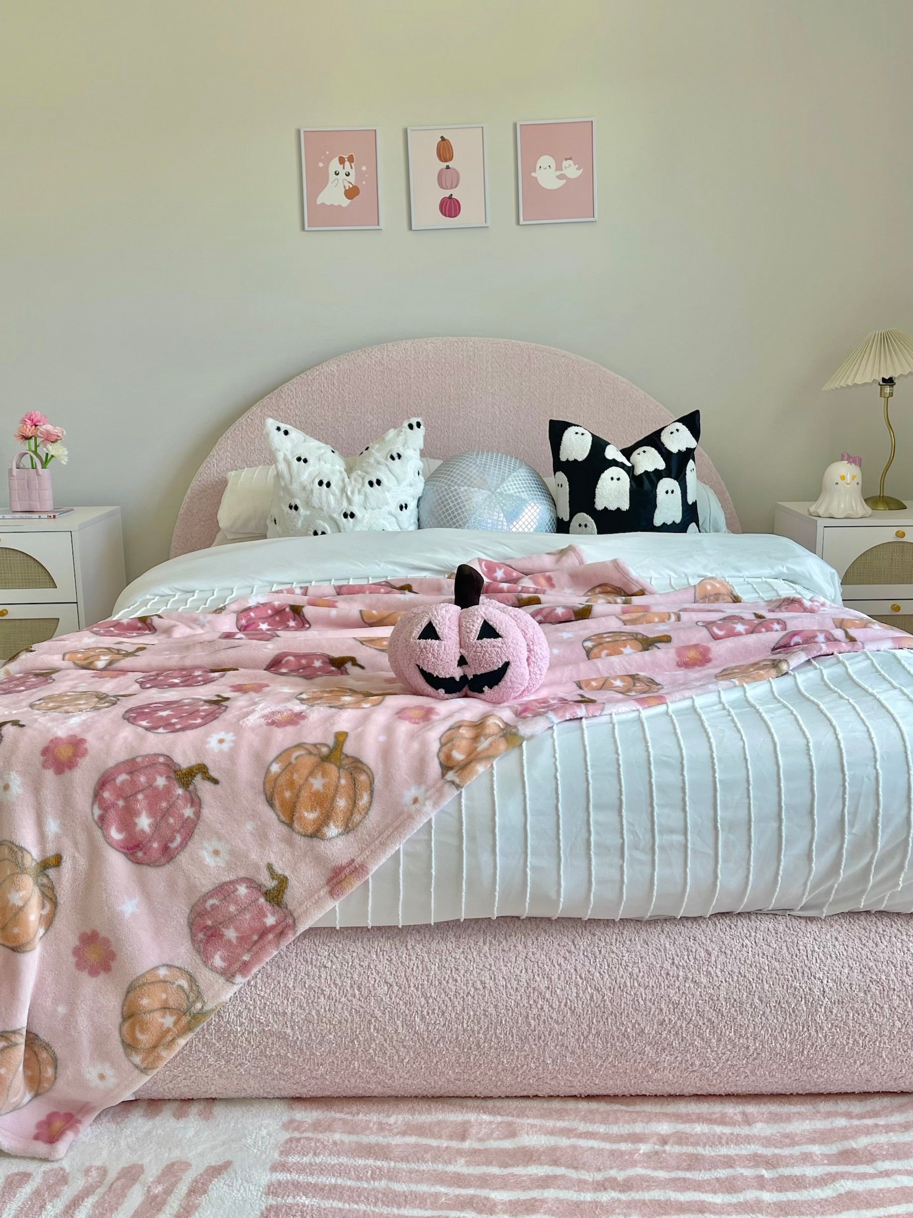 Children's bedroom with a bed covered in a pink blanket with pumpkins and ghosts, surrounded by Halloween-themed decor.