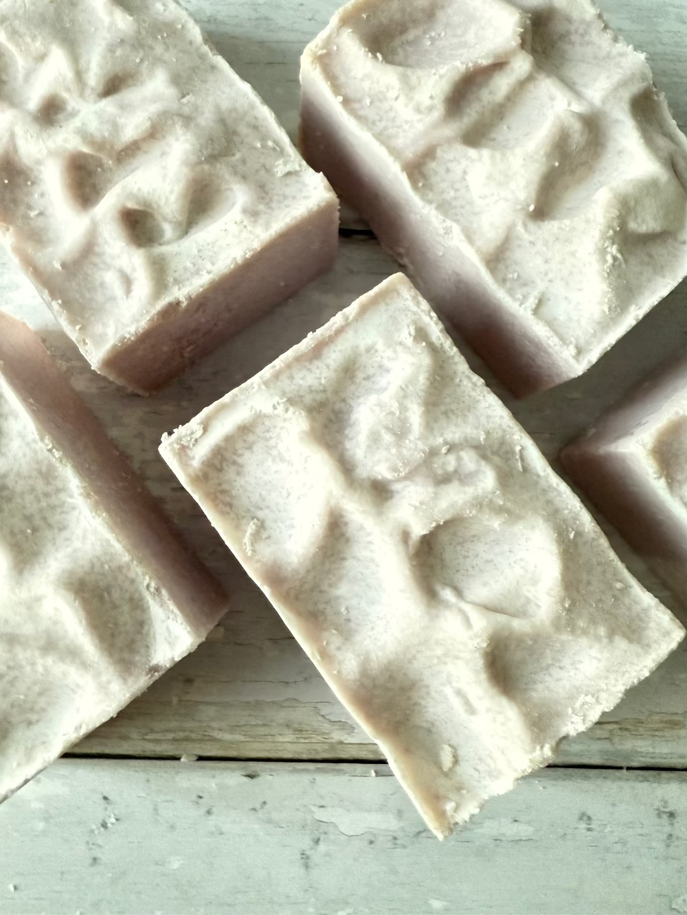 Four rectangular bars of soap with a textured surface on a light wooden background