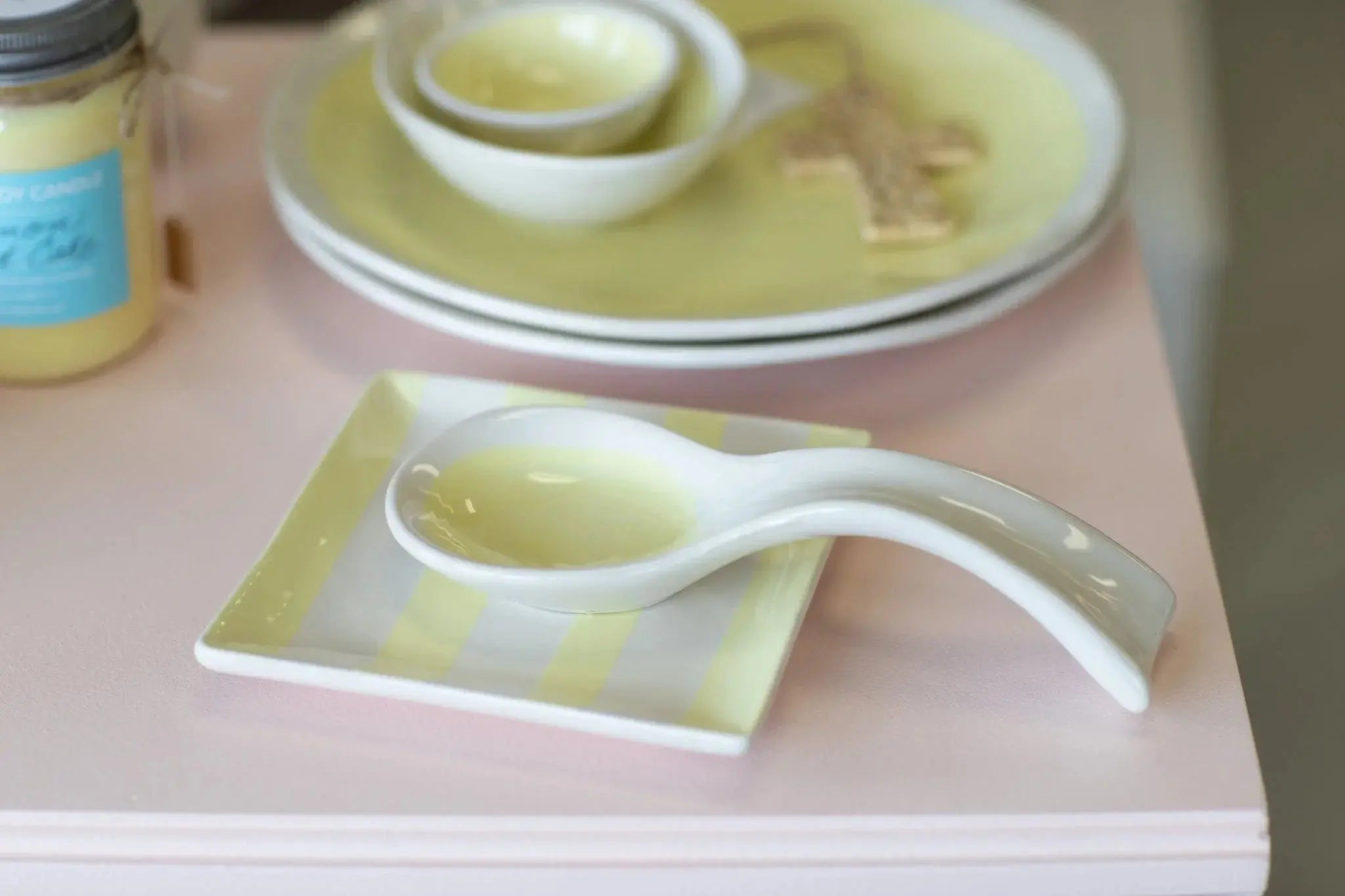 White ceramic spoon rest on yellow striped tray, farmhouse kitchen decor with candle and plates