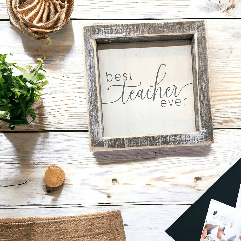 Decorative sign with 'best teacher ever' text in a rustic wooden frame on a wooden surface.