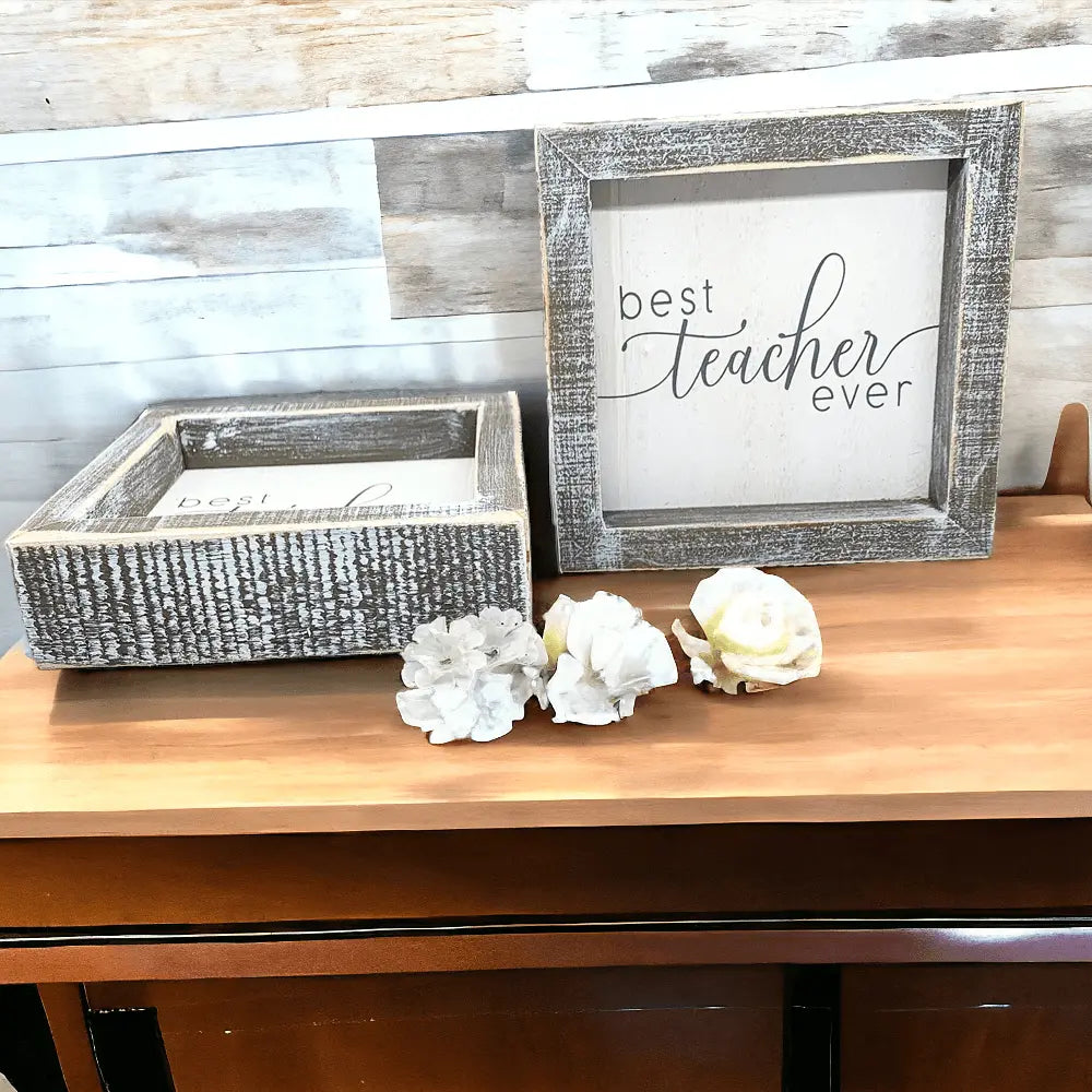 Decorative wooden box and framed sign on a wooden surface with flowers.