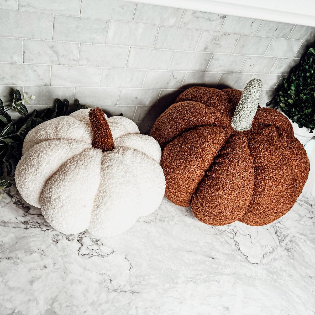 Two textured pumpkins, one white and one brown, on a marble surface with a tiled wall background.